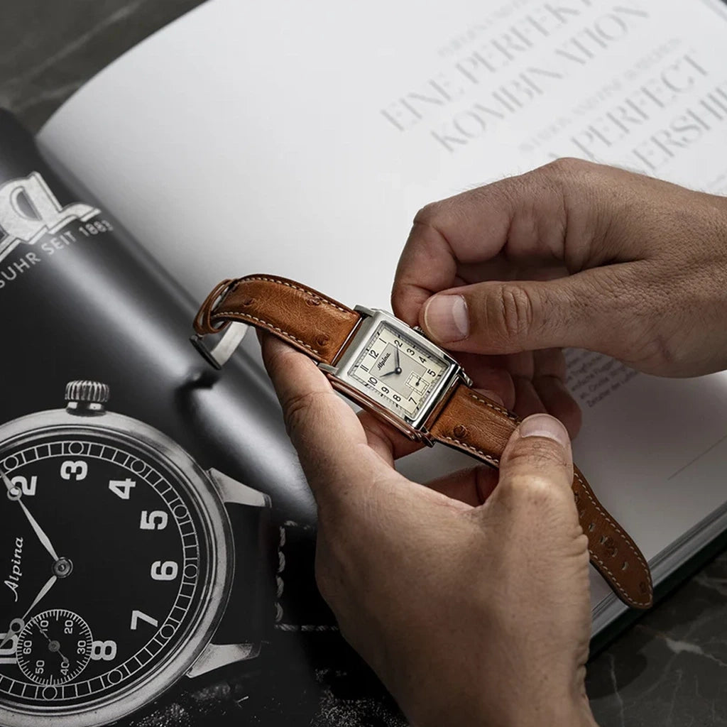 Alpina Heritage Carree Automatic 140 Years rektangulær herreklokke med lys tallskive, kasse i stål og rem av strutseskinn.